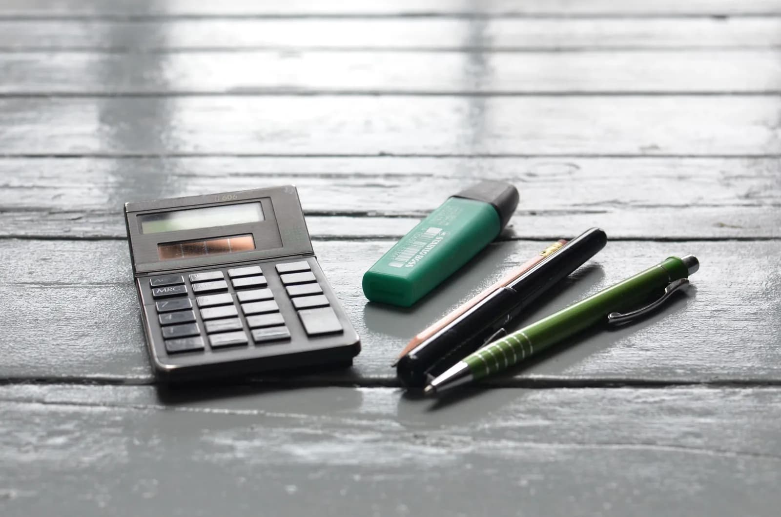 Calculadora y bolígrafos sobre una mesa de madera